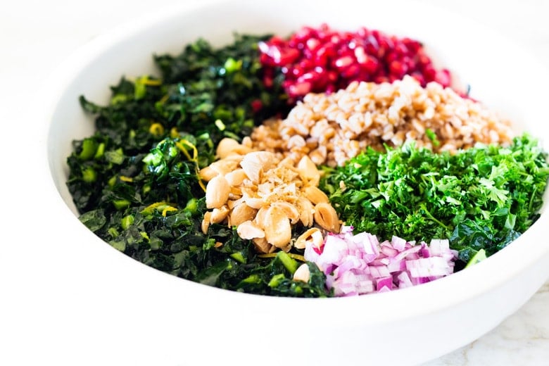 salad bowl with farro salad with kale, almonds and pomegranate seeds, red onion, and parsley.