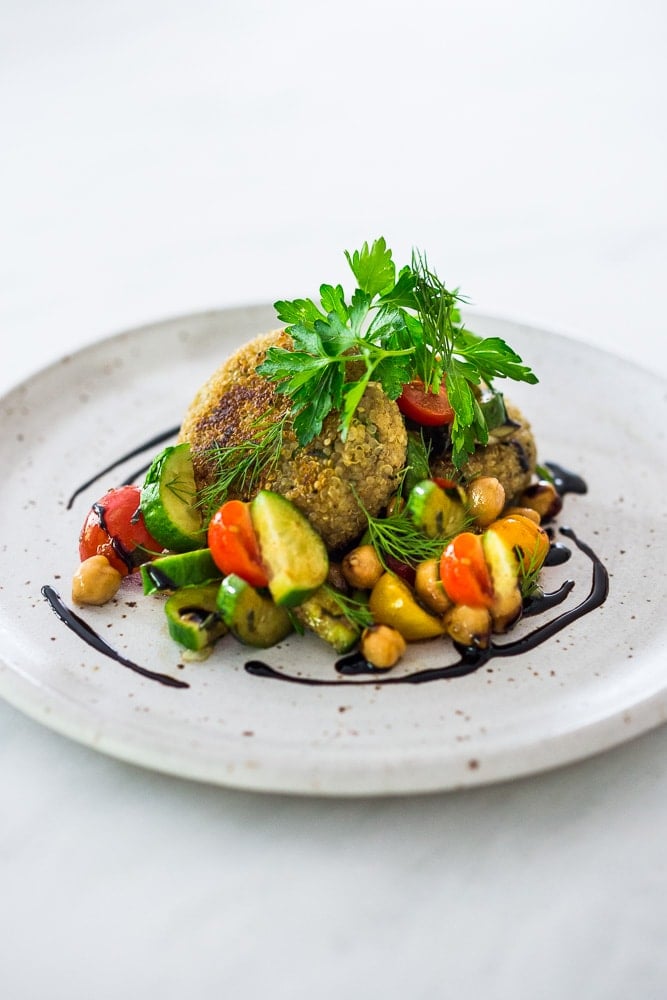 Quinoa cakes topped with tomato chickpea relish on a white plate with balsamic drizzle. 