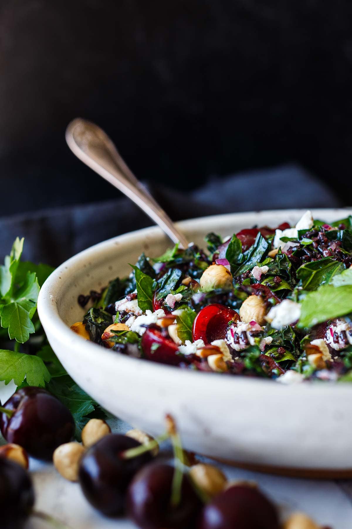 cherry salad with kale and black rice, hazelnuts, goat cheese, and red onion in serving bowl with serving spoon.