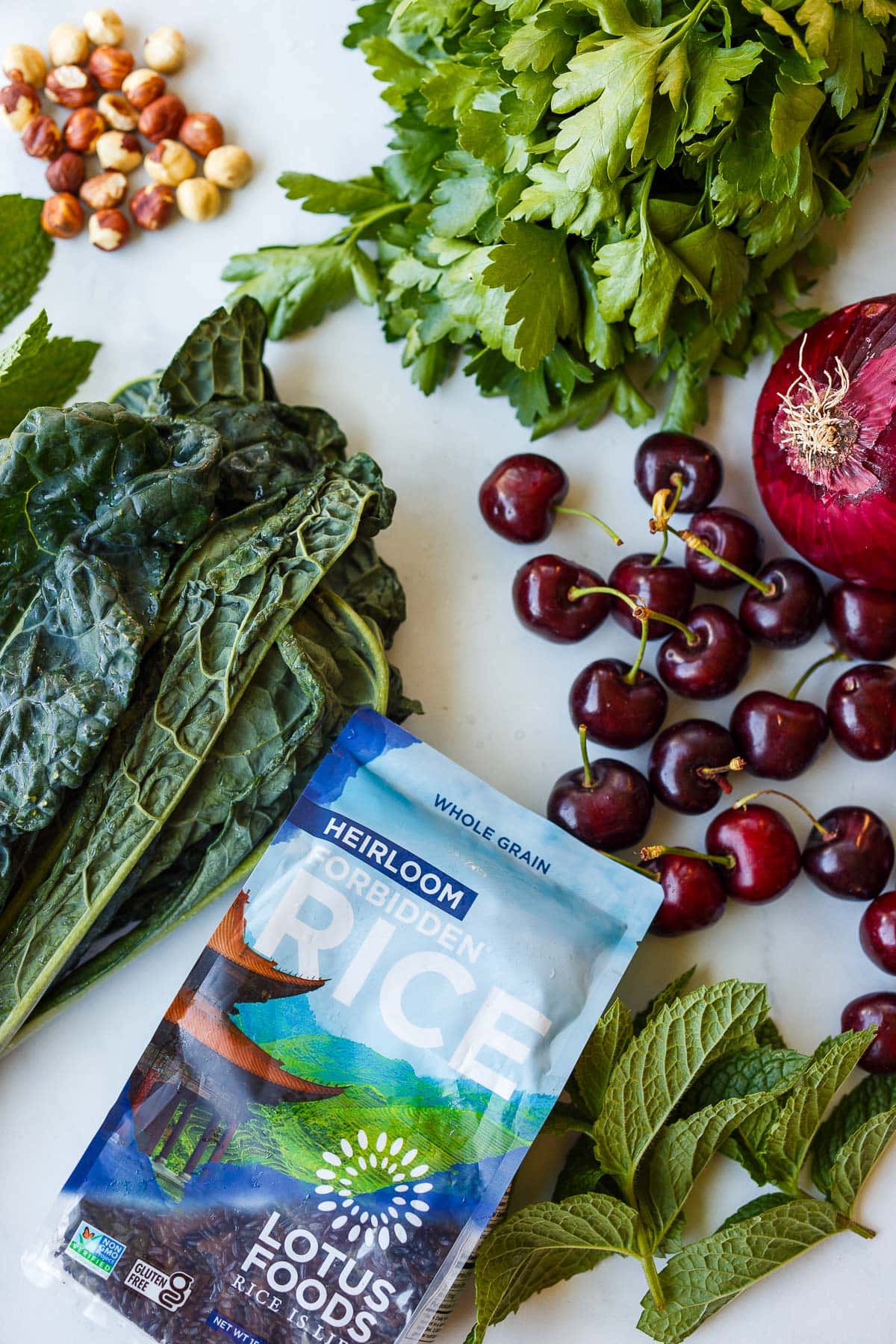ingredients laid out for cherry salad - hazelnuts, parsley, mint, lacinato kale, red onion, cherries, black rice. 