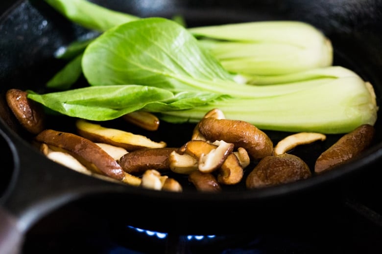 bok choy and shiitakes sautéing in a cast iron skillet.