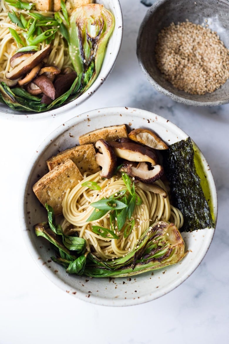 two bowls of ramen noodles, seared bok choy and shiitake mushrooms, crispy tofu, kombu, and scallions, with sesame seeds on top.