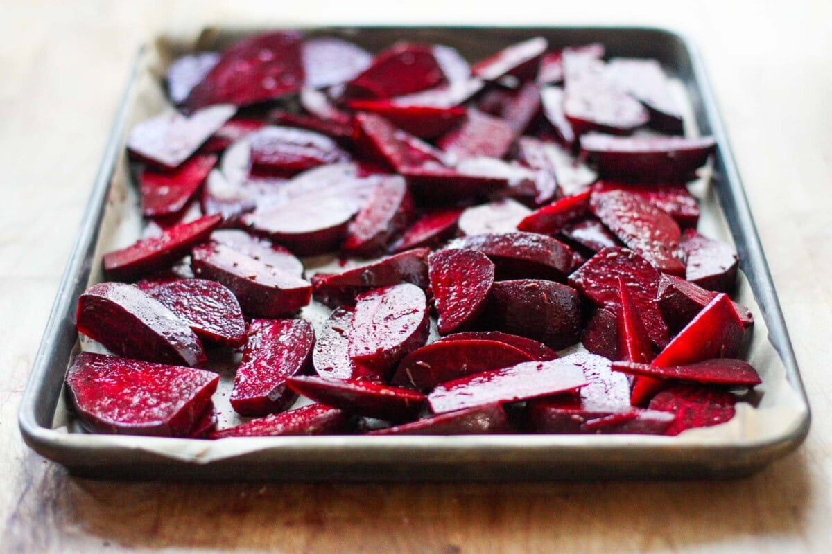 parchment lined baking sheet with sliced beets seasoned and spread out evenly.