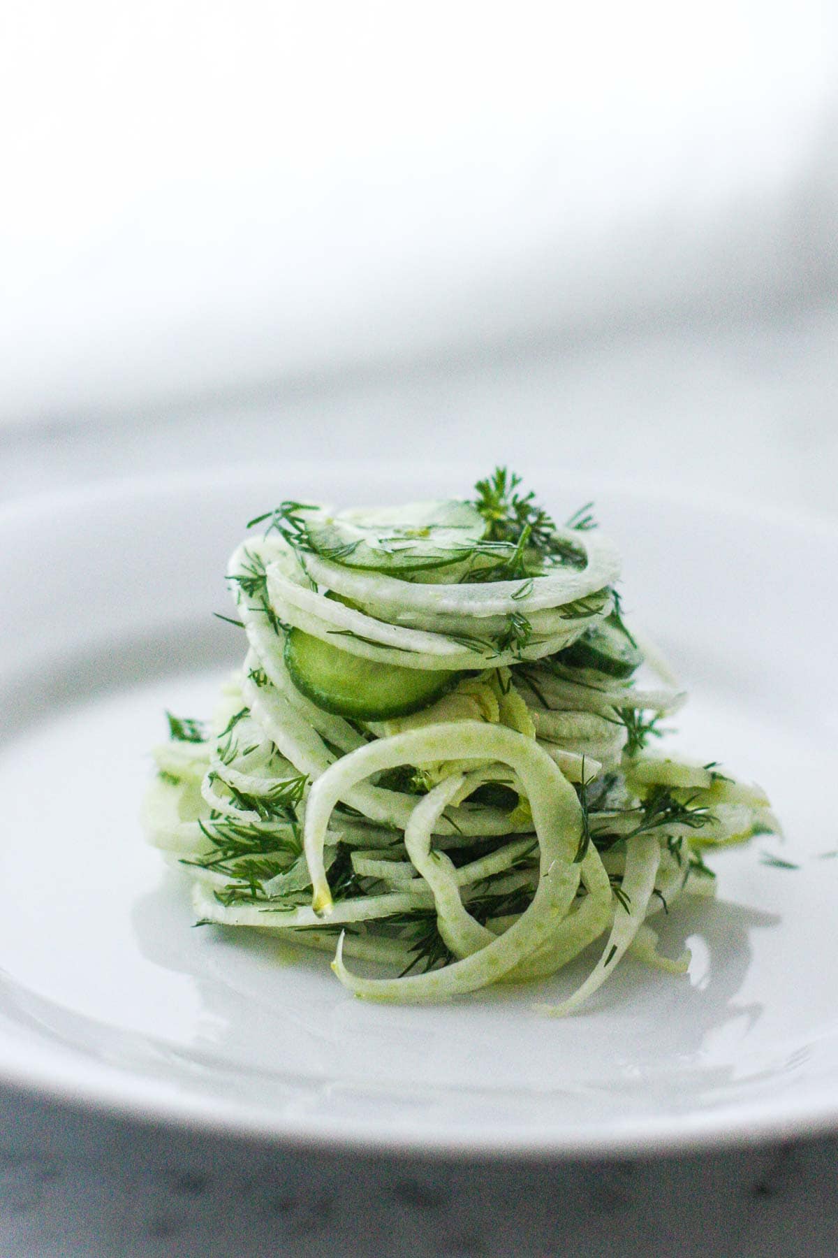 Shaved Fennel salad with cucumber and dill, stacked high on a white serving plate. 