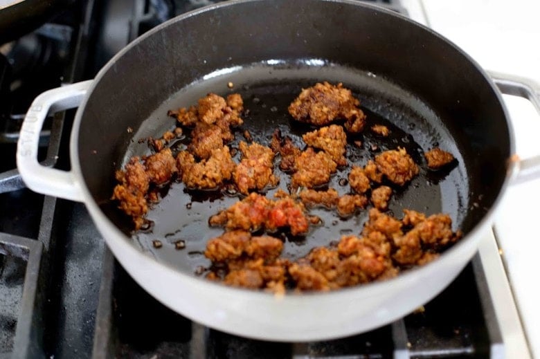 Chorizo browning in a pan on the stove.