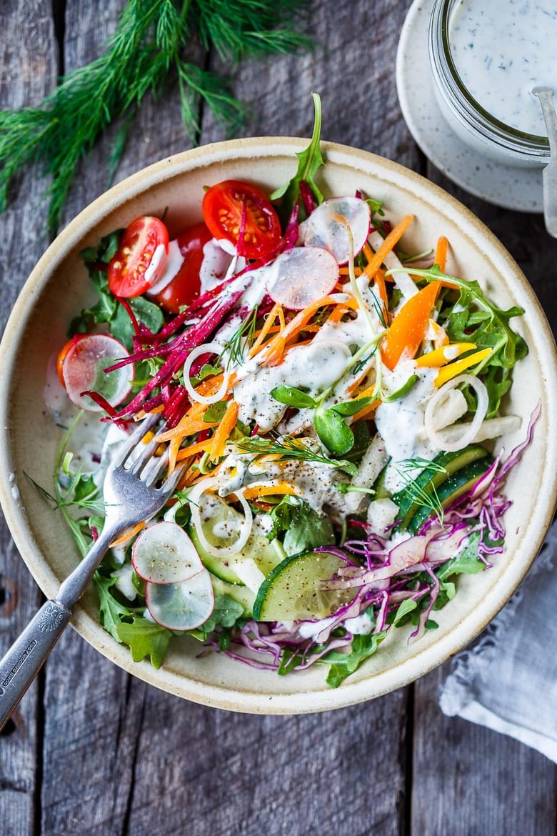 Rainbow salad in a bowl with dressing and a fork.