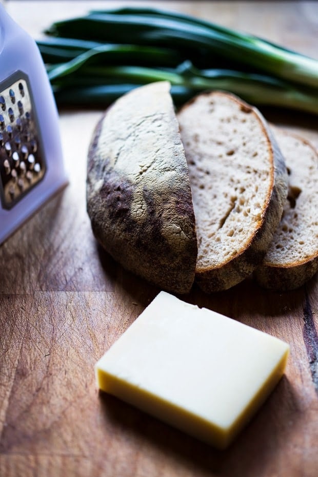 wood board with block of gruyere cheese, slices of bread, and box grater. 