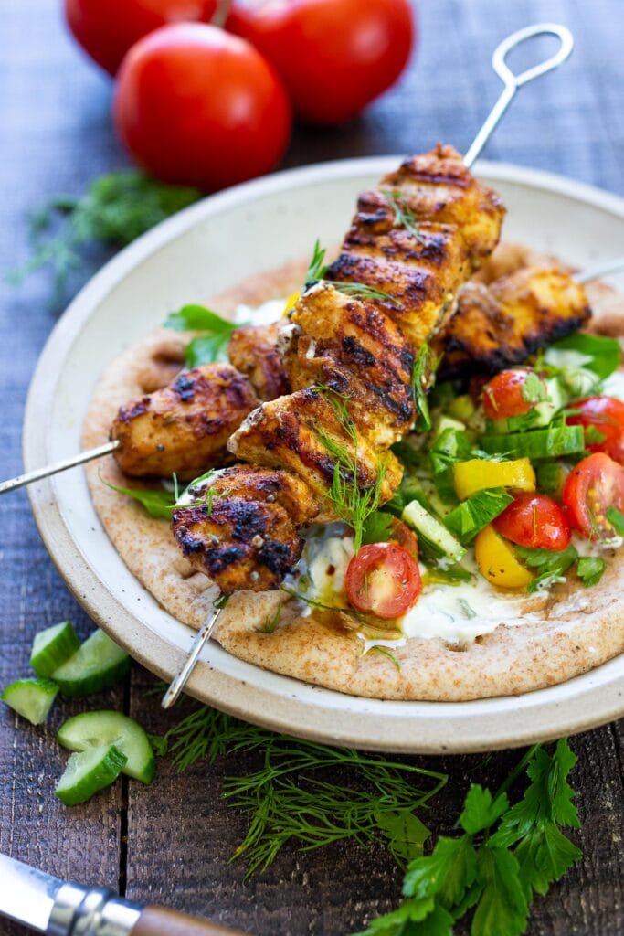 grilled chicken shawarma on skewers in naan bread with cucumber tomato dill salad and tzatziki.