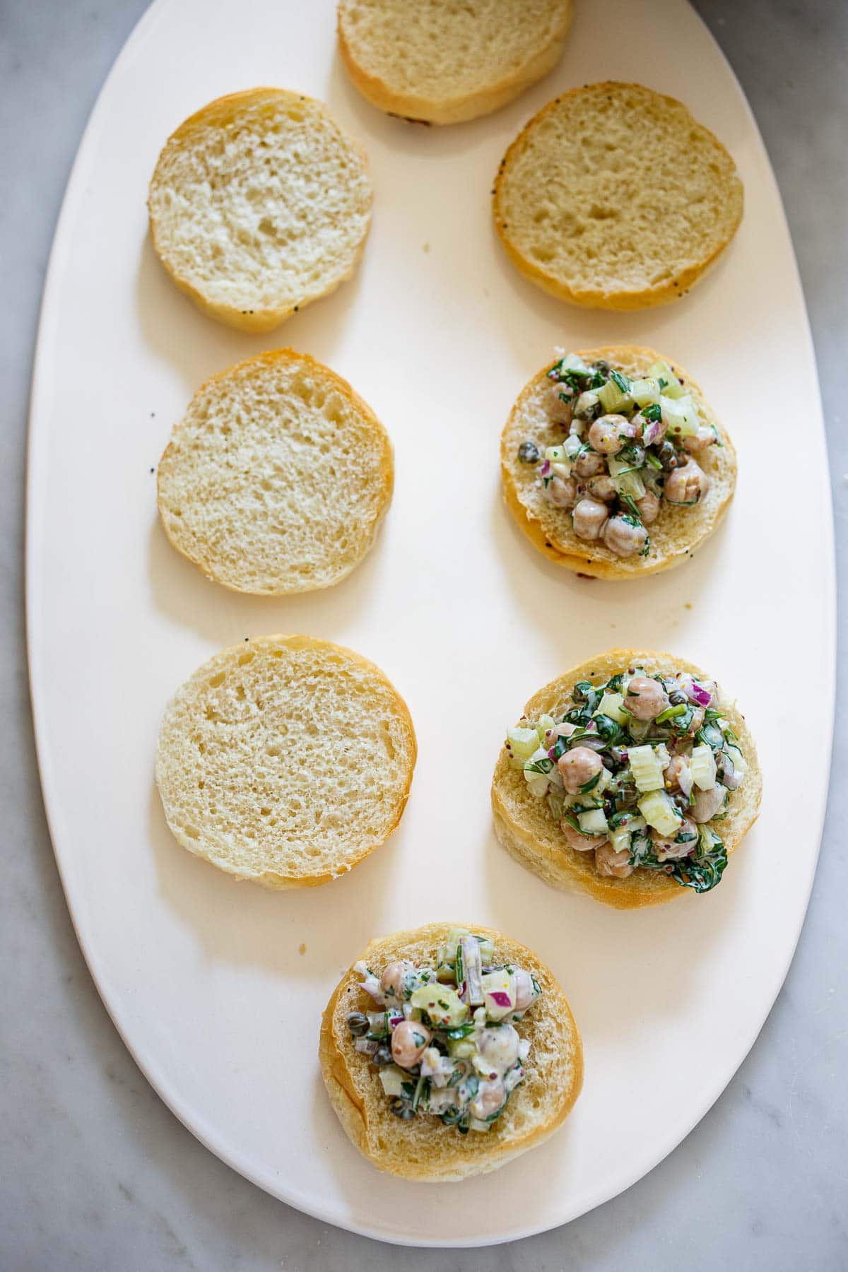 serving platter with slider bun bottoms with three topped with chickpea salad. 