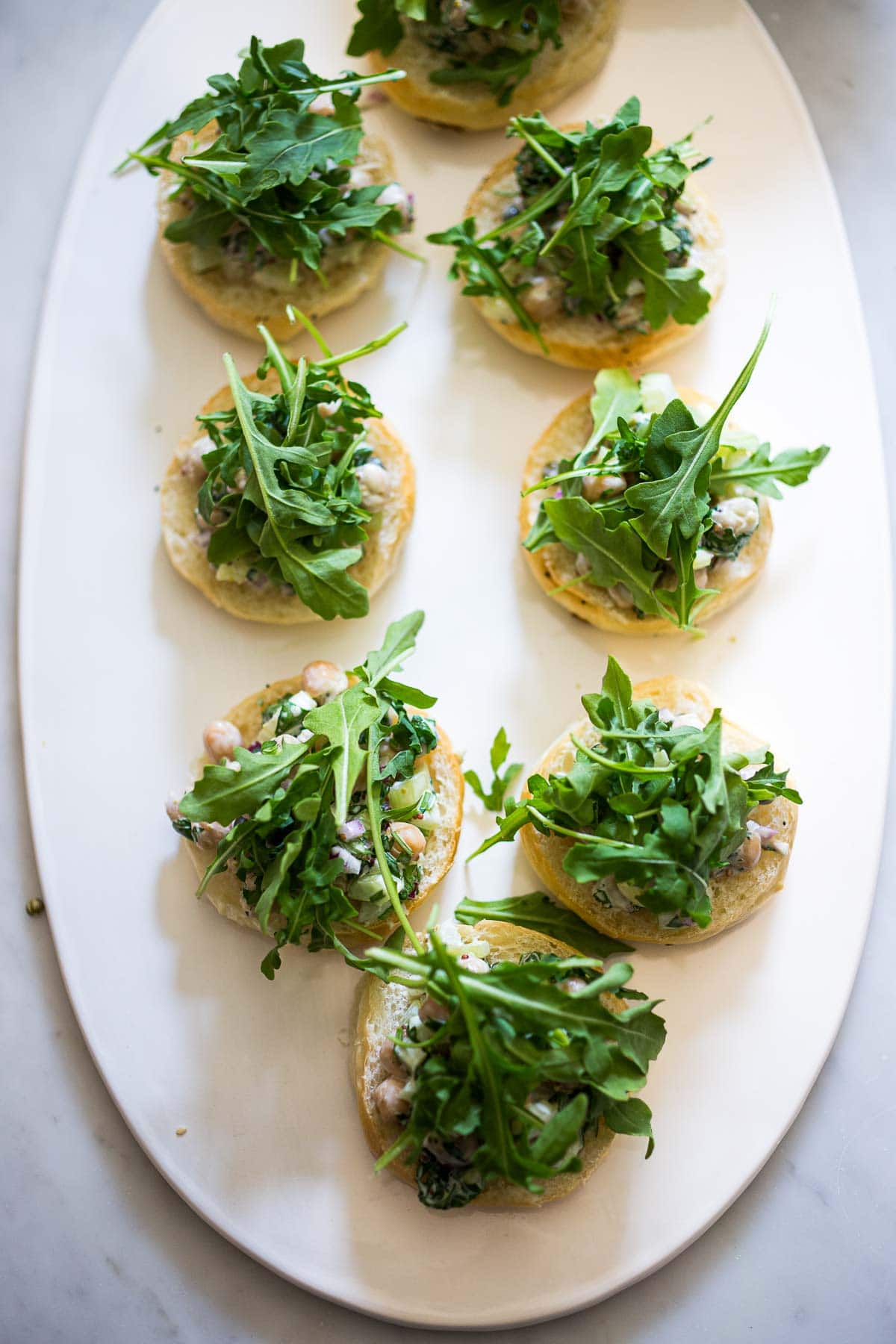serving platter with slider bun bottoms, topped with chickpea salad and fresh arugula. 