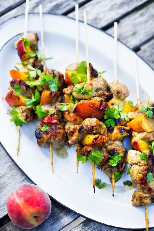 grilled jerk chicken and peach skewers stacked on serving plate topped with cilantro.