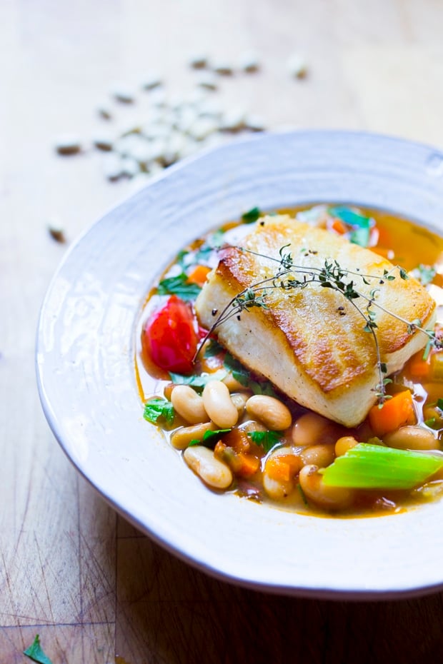 A simple healthy Mediterranean recipe for Sea Bass served over a fragrant Cannellini Bean Stew. Can be made in 30 minutes! | www.feastingathome.com #seabass #cannellinibeans