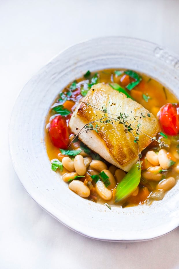 A simple healthy Mediterranean recipe for Sea Bass served over a fragrant Cannellini Bean Stew. Hearty and flavorful this easy dinner can be made in 30 minutes! #seabass #cannellinibeans