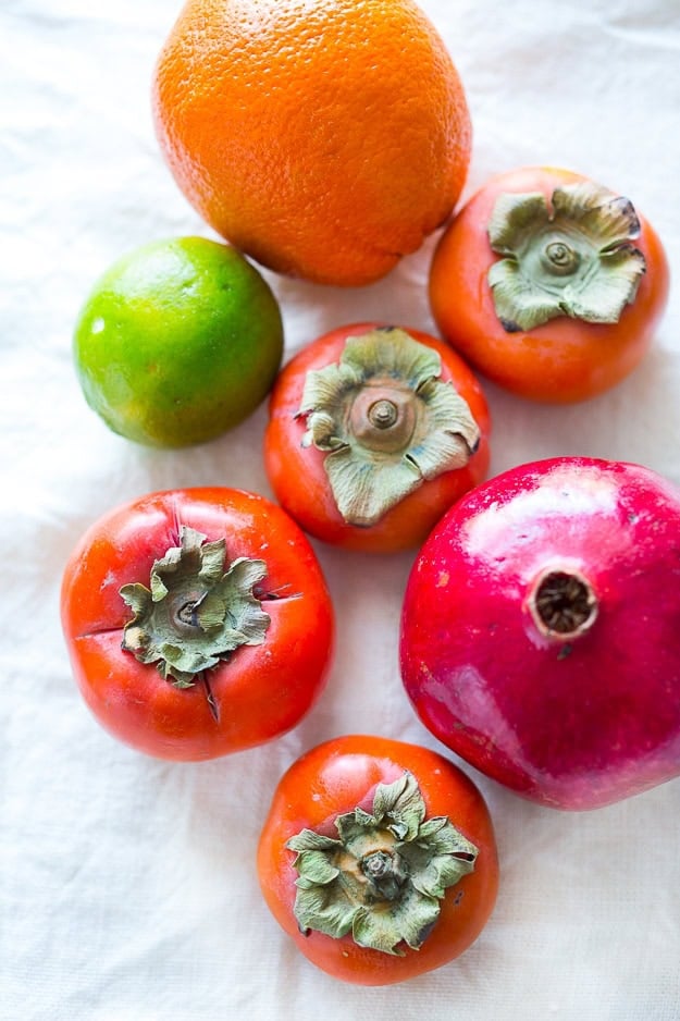 Persimmon, pomegranate and shaved fennel salad with honey citrus dressing. vegan, gf | www.feastingathome.com persimmon salad ingredients - orange, lime, persimmons, and pomegranate laid out on linen fabric.