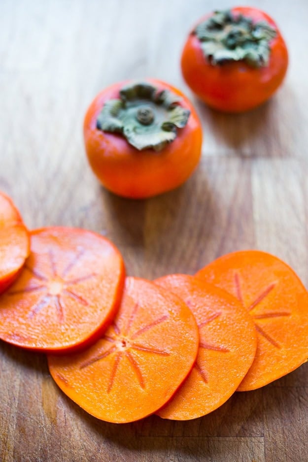 Persimmon, pomegranate and shaved fennel salad with honey citrus dressing. vegan, gf | www.feastingathome.com thinly sliced persimmon on wood cutting board.
