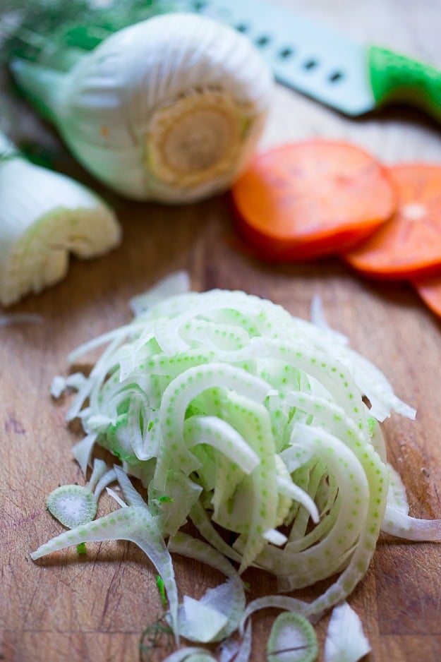 thinly sliced fennel on wood cutting board.