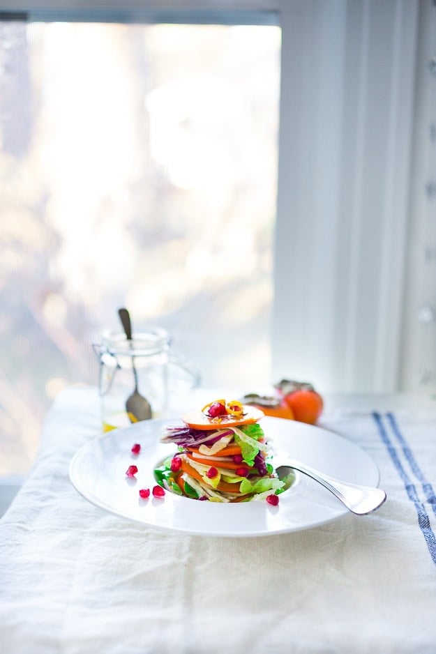 Persimmon, pomegranate and shaved fennel salad with honey citrus dressing. vegan, gf | www.feastingathome.com serving plate with persimmon salad stacked in a tower with butter lettuce, fennel, and pomegranate seeds.