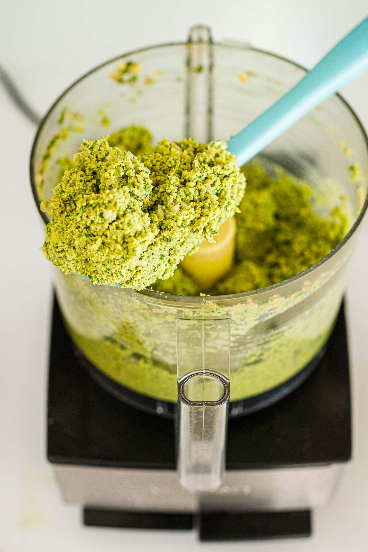 spatula holding up falafel burger mixture above food processor.