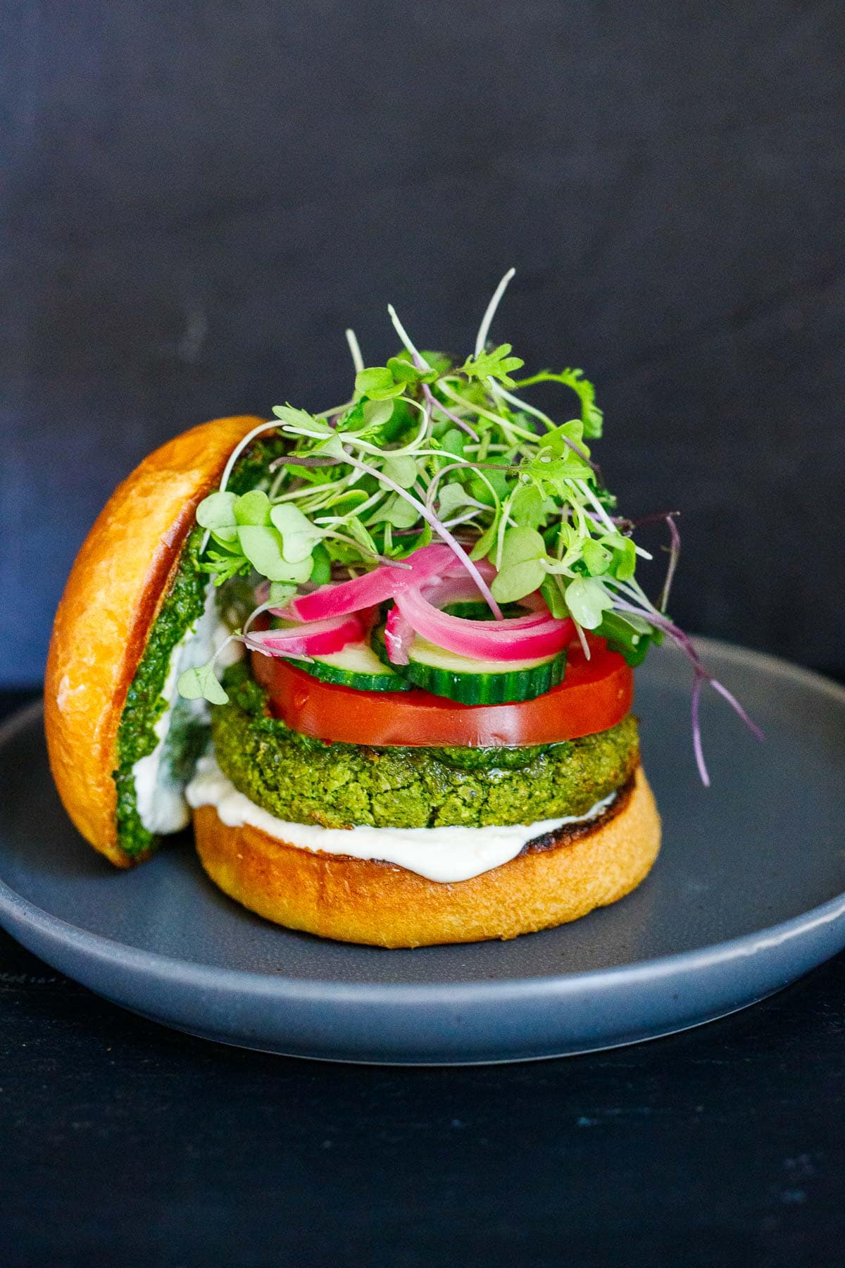 A falafel burger with tahini yogurt, pickled onions, tomatoes, cucumber on a toasty bun.