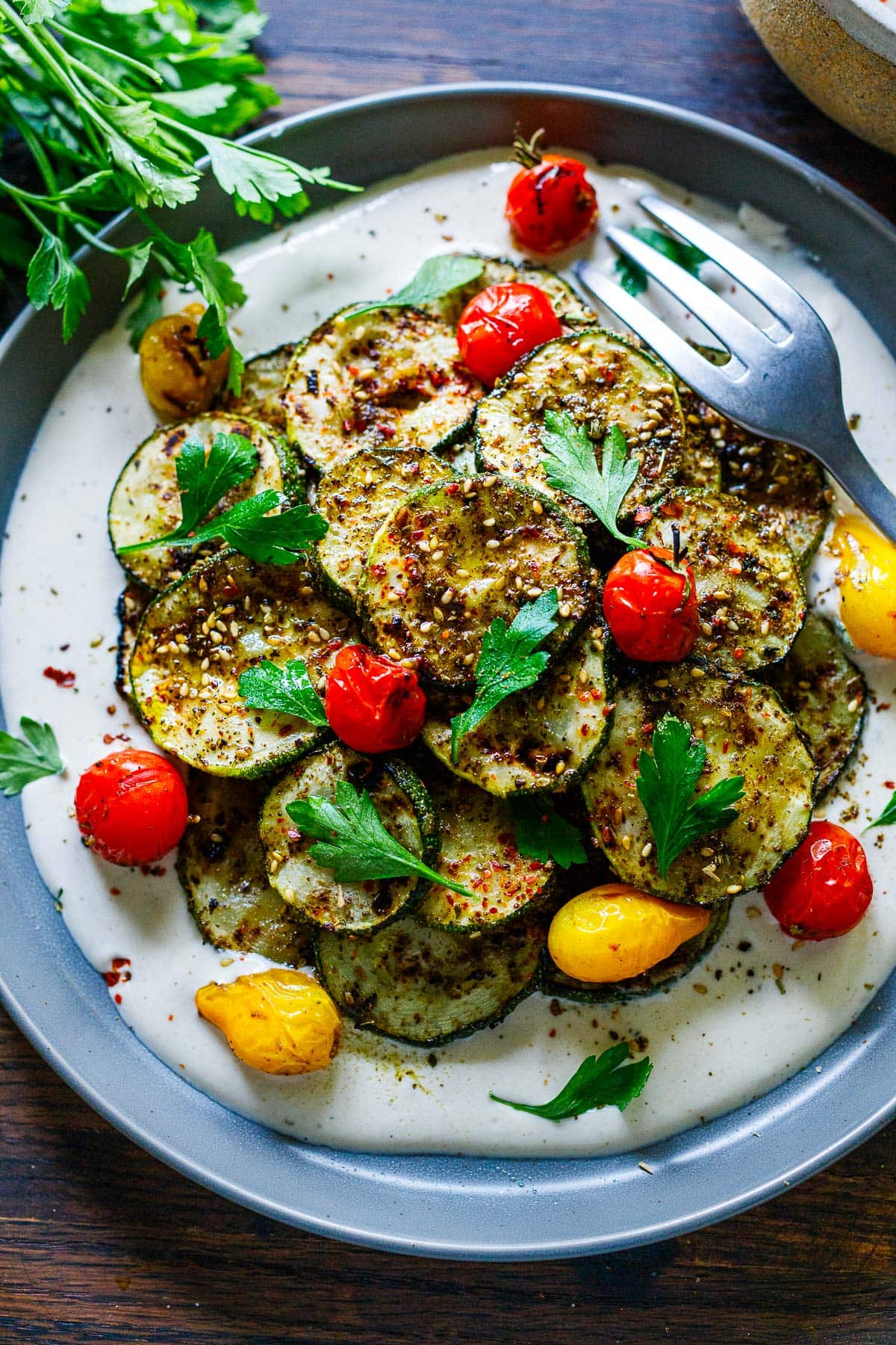 grilled zucchini on a plate with zaatar spice, tomatoes and tahini yogurt.