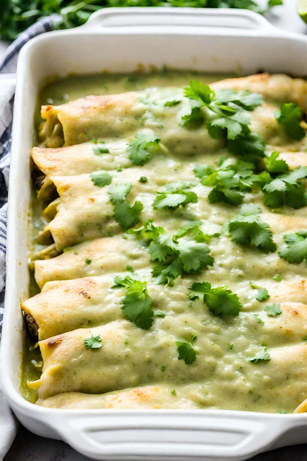 baking dish with enchiladas verde, topped with cheese and green enchilada sauce, garnished with cilantro.
