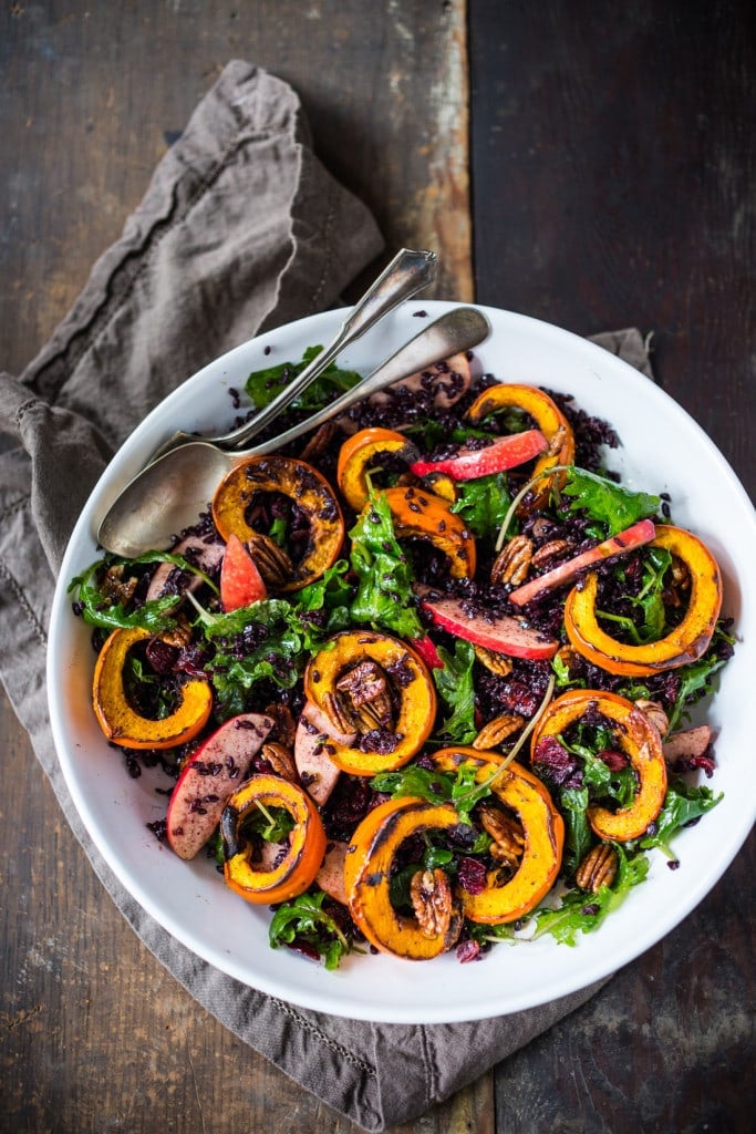 roasted pumkin salad roasted pumpkin salad with baby kale, sliced apples, and black rice in white bowl with serving utensils.
