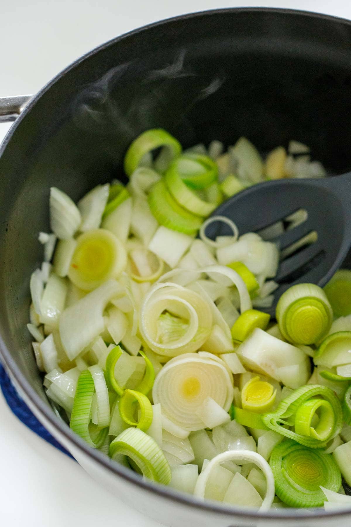 sliced leeks and onions sautéing in pot.