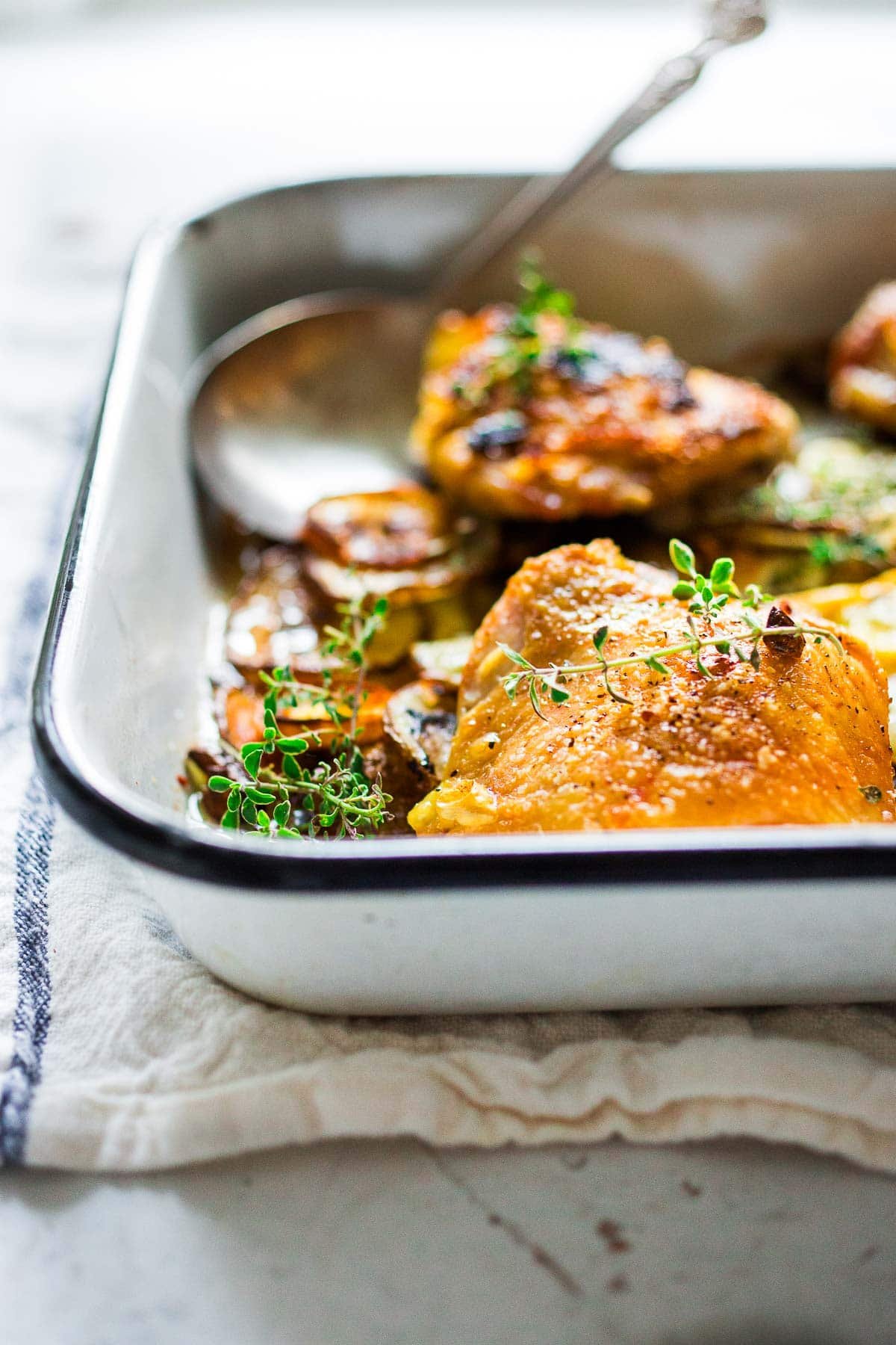 Oven-baked chicken thighs, roasted over thinly sliced potatoes with garlic, lemon and thyme. 
