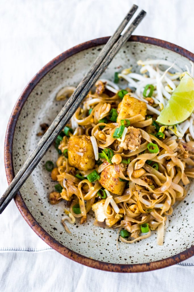 pad thai in a bowl with chopsticks and lime. 