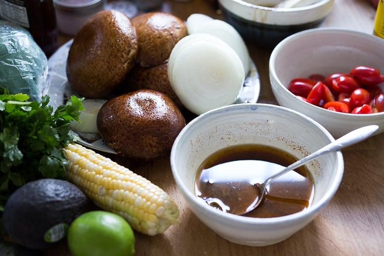 ingredients laid out for grilled mushroom salad- dressing, tomatoes, onions, mushrooms, corn, lime, and avocado.