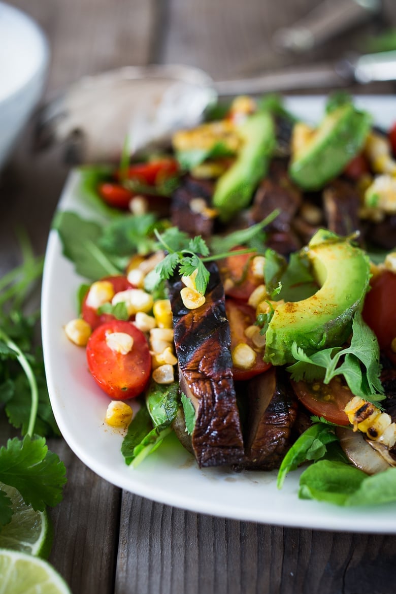 serving platter with grilled portobello salad topped with avocado slices, cron, and cherry tomatoes.