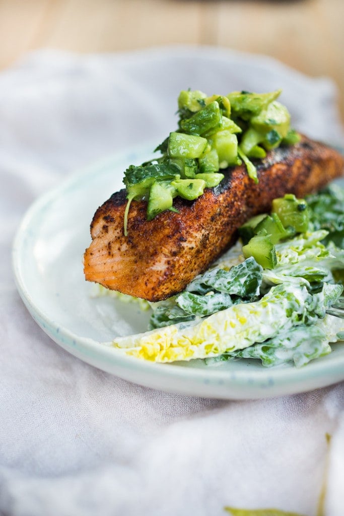 Mexican grilled salmon topped with avocado cucumber salsa over plate of greens in creamy cilantro lime dressing.