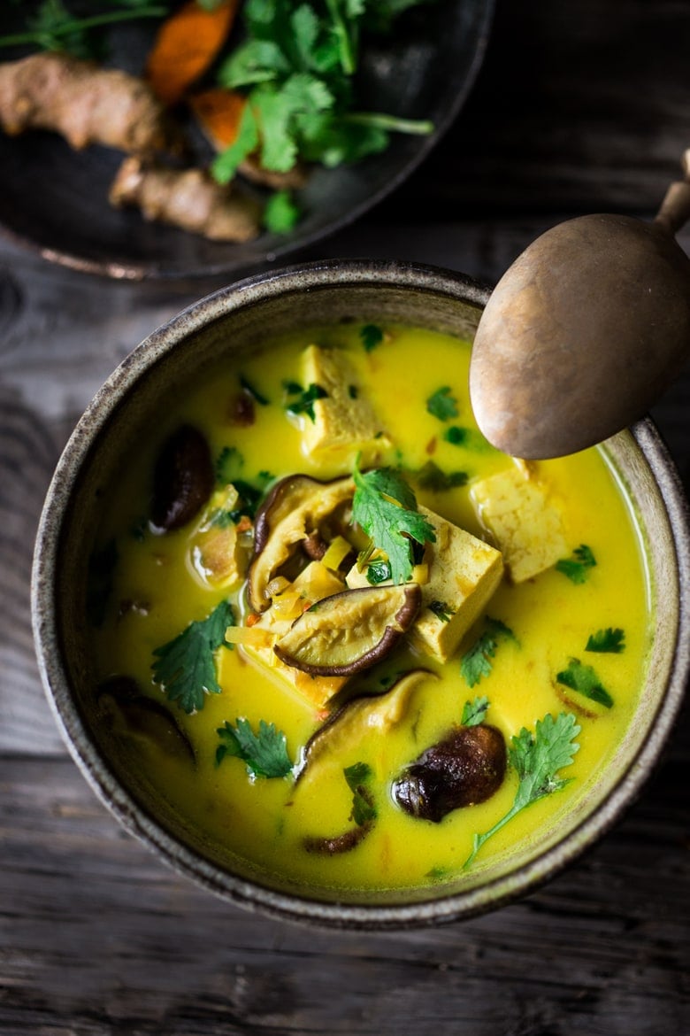 bowl with coconut tofu curry with shiitake mushrooms and cilantro and a spoon leaning on the bowl. 