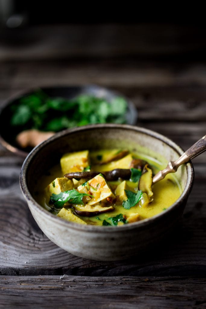 coconut turmeric tofu curry in bowl with spoon, with shiitake mushrooms and cilantro.