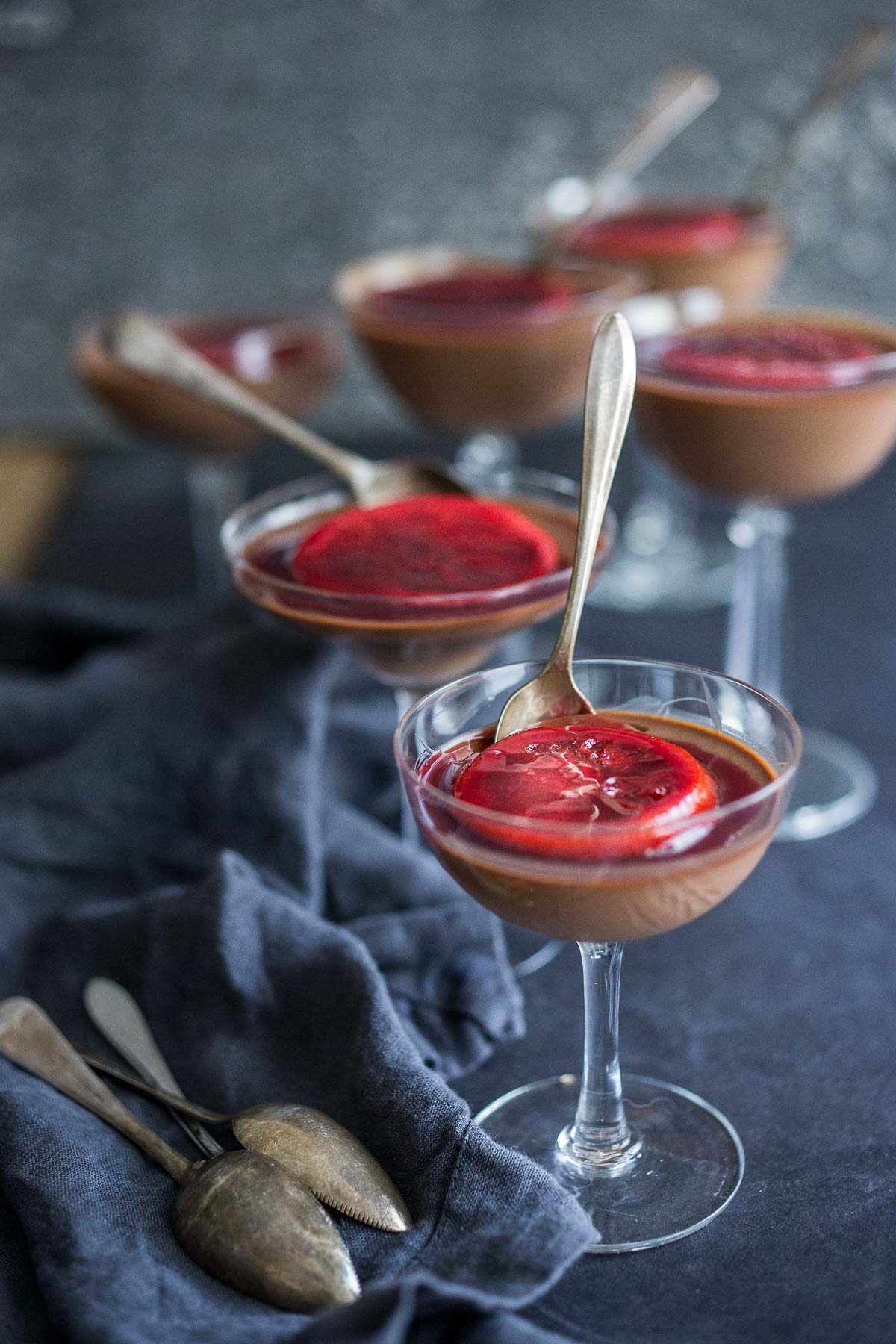 panna cotta in glasses with serving spoons topped with candied blood orange slice. 