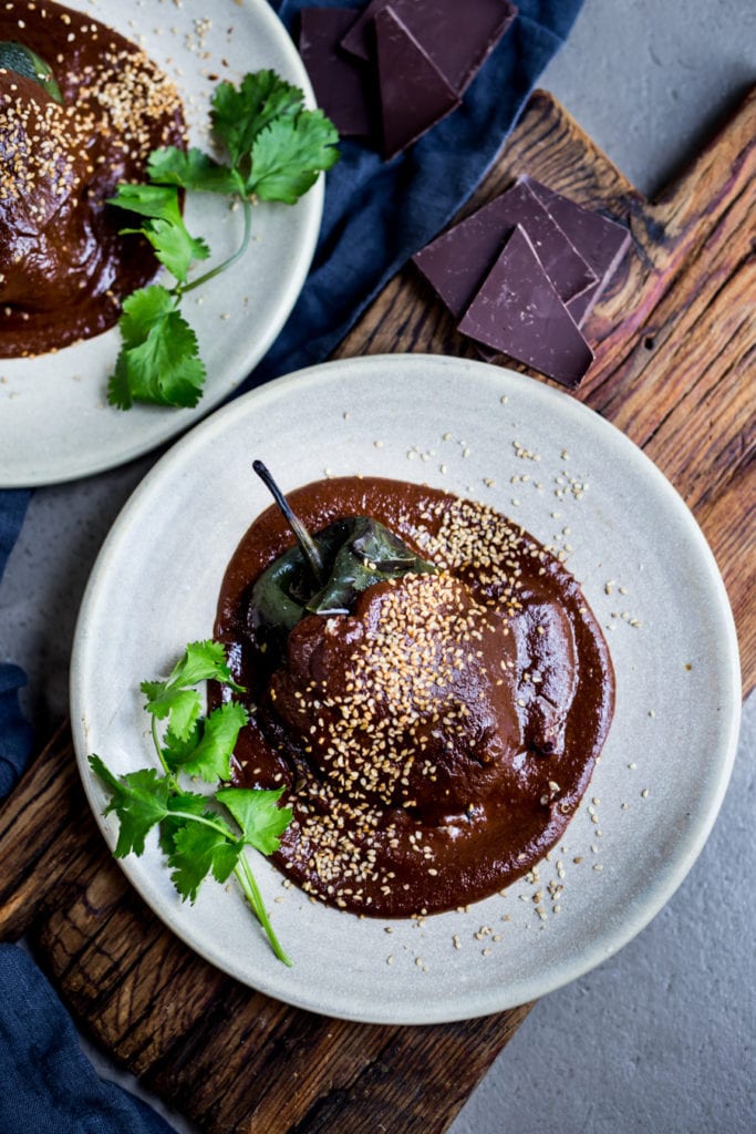 Quinoa stuffed poblano peppers with mole negro sauce, on a white plate with sesame seeds. 