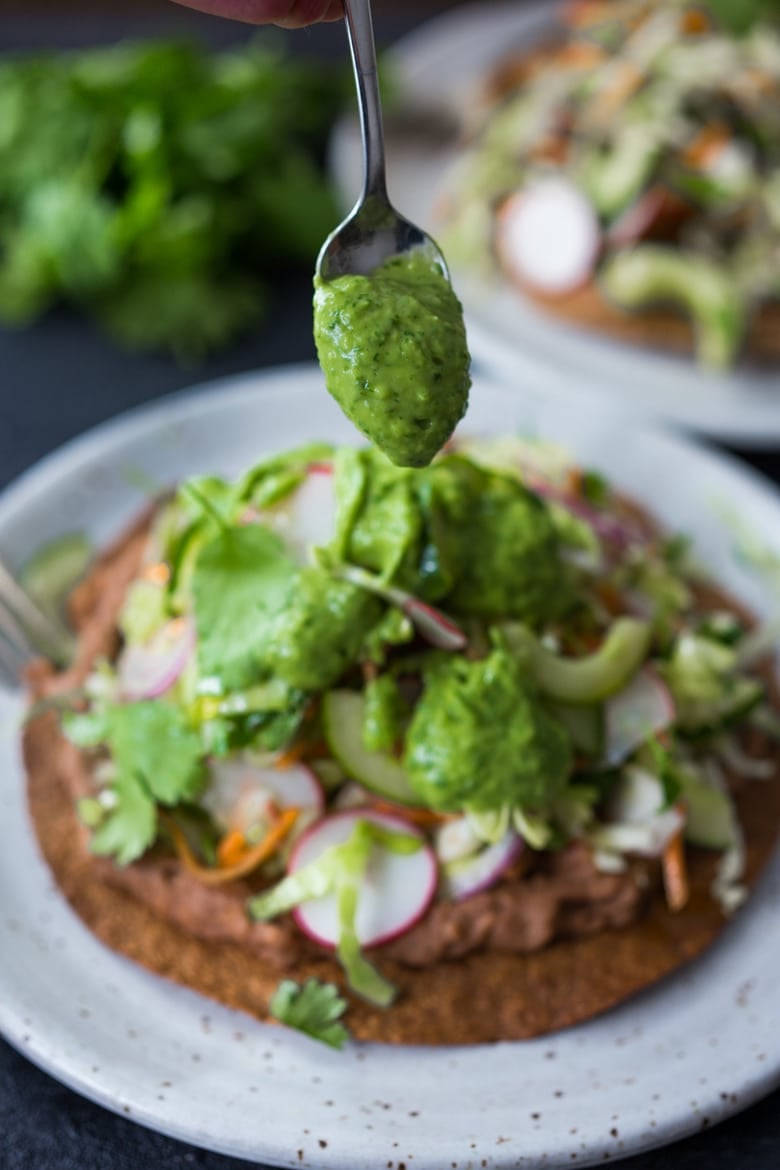 Introducing Tlayudas! Traditional Oaxacan street food, tlayudas are a cross between a tostada and a pizza, made with a crispy tortilla, topped with refried beans, cheese (optional) cabbage slaw, avocado and cilantro. This healthy version is vegan and GF adaptable! | #tlayudas #tostadas #mexicanpizza #vegan #oaxacanfood #mexicanstreetfood #veganmexican #healthymexicanrecipes | www.feastingathome.com