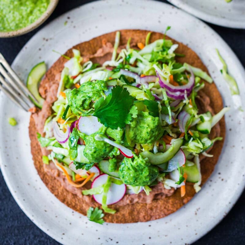 How to make Tlayudas! This healthy, lightened-up, version is vegan and GF adaptable! Feel free to add walnut chorizo,  chicken carnitas or turkey chorizo! Made with a crispy tortilla, topped with refried beans, cheese (optional) cabbage slaw, avocado and cilantro.
