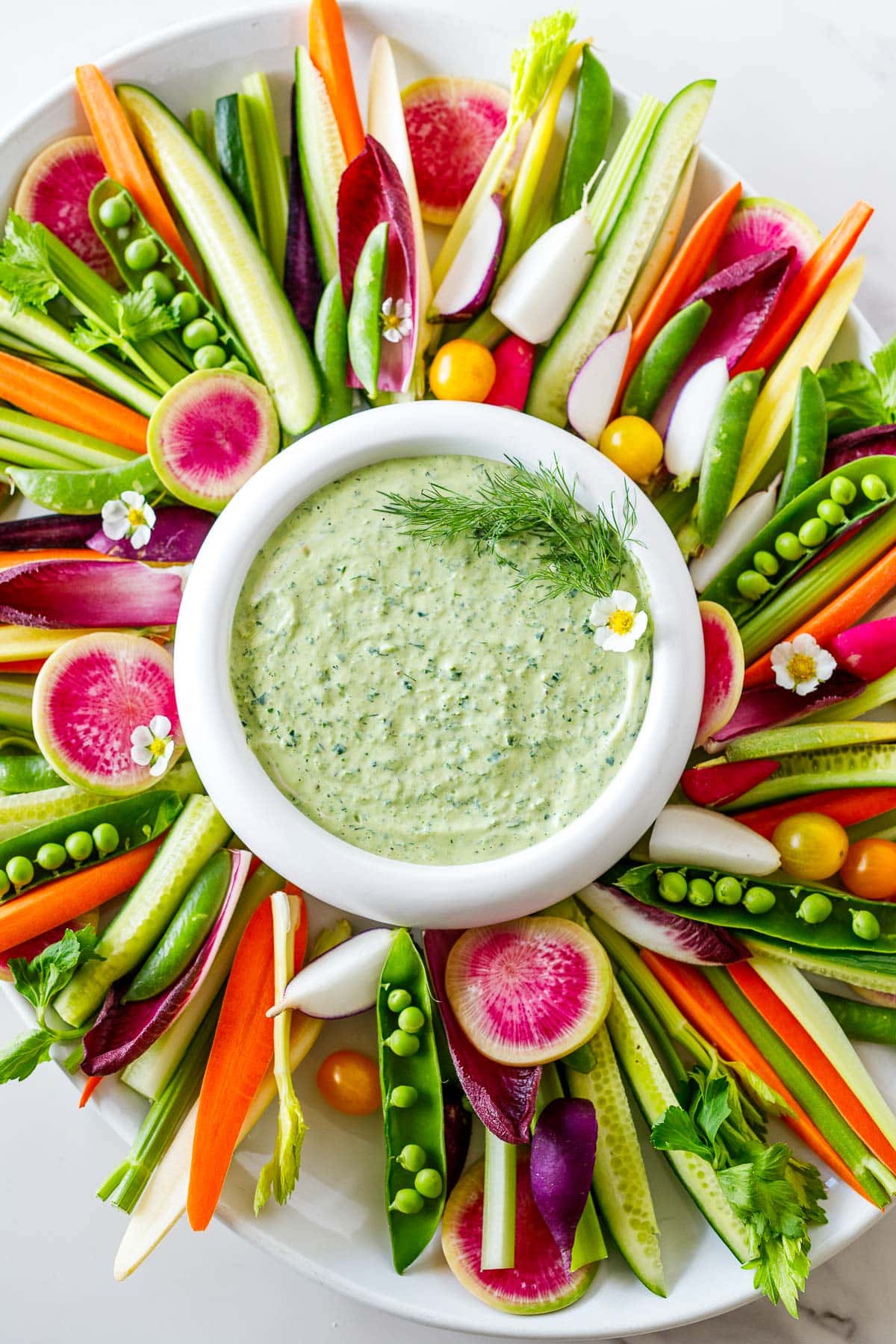 A crudité platter with green goddess dressing on a white counter. 