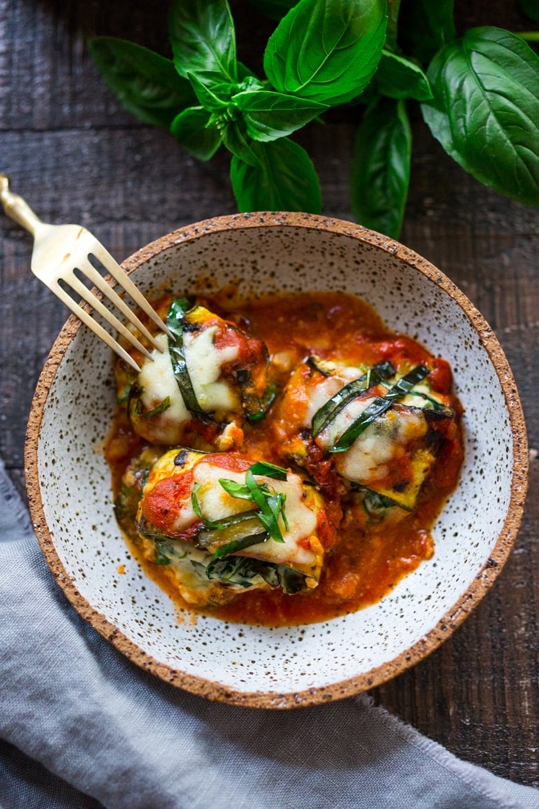 bowl with three zucchini lasagna roll ups garnished with basil.