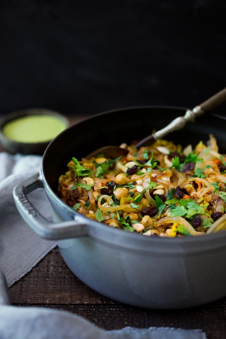 Vegetable biryani in a dutch oven with onions, raisins and coriander leaves. 