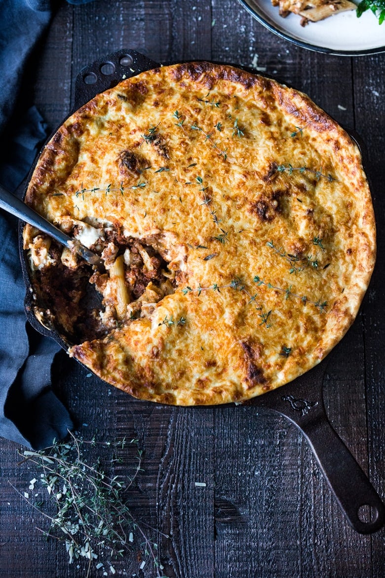 skillet with pastitsio (baked Greek pasta with lamb), spoon dipping into skillet to show pasta and lamb bolognese underneath.