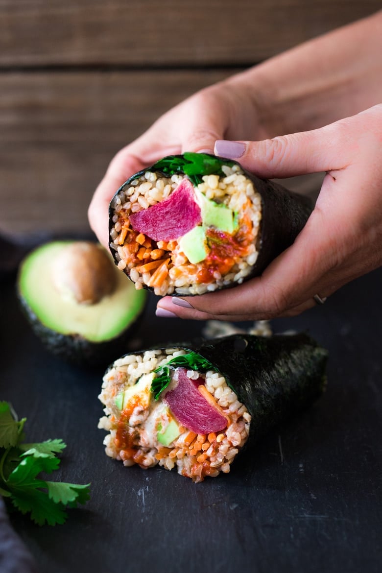 hands holding a sushi burrito with ahi tuna, sushi rice, and avocado. 
