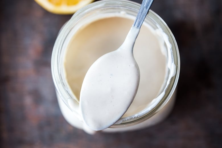 creamy tahini sauce in jar with spoon on top.