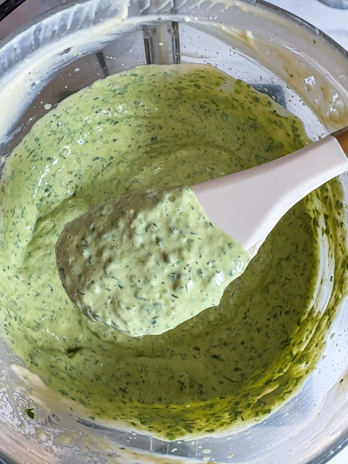 food processor with green goddess dressing and a white spatula lifting some of the dip up to reveal texture. 