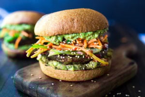 This Asian-style, grilled, vegan portobello mushroom burger is full of delicious umami flavor! It's lathered with Asian-style Guacamole, topped with a cool cucumber ribbon salad and crunchy carrot slaw. Healthy, delicious and really satisfying. AND totally vegan! #veganburger #portobelloburger #veganportobelloburger #portobellomushroomrecipes #portobello #vegan #veganburger #grilled #grilledportobello
