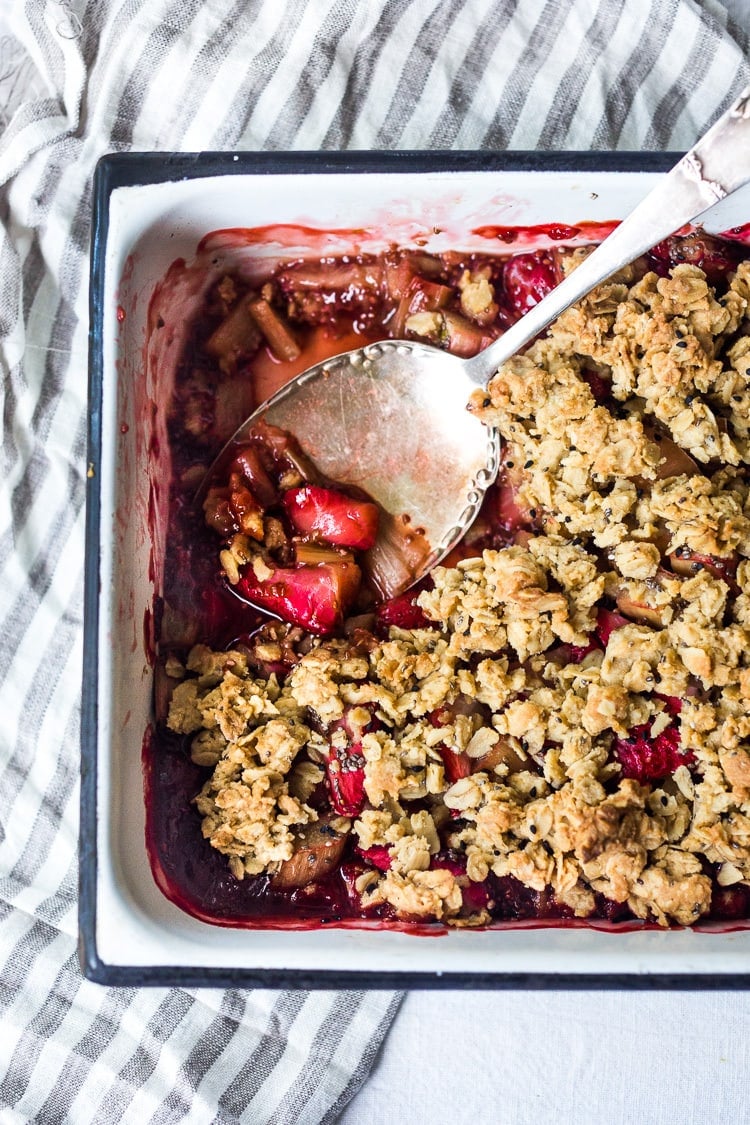 baking dish with strawberry rhubarb crisp with spoon scooping up juicy filling.