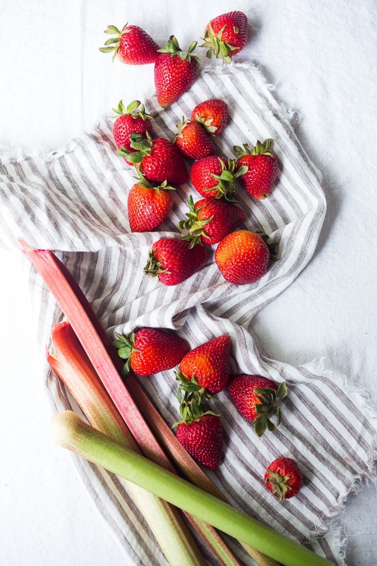 fresh whole strawberries and rhubarb stalks on kitchen cloth.