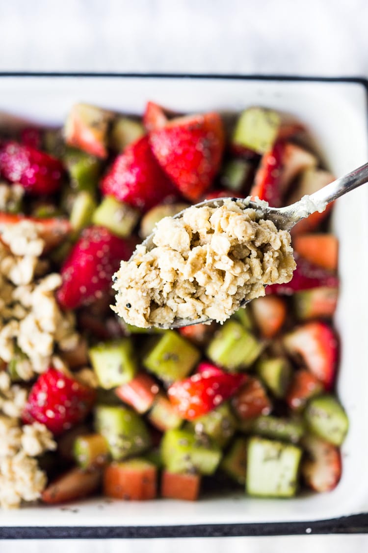 spoon dropping oat crumble topping over strawberry rhubarb filling. 
