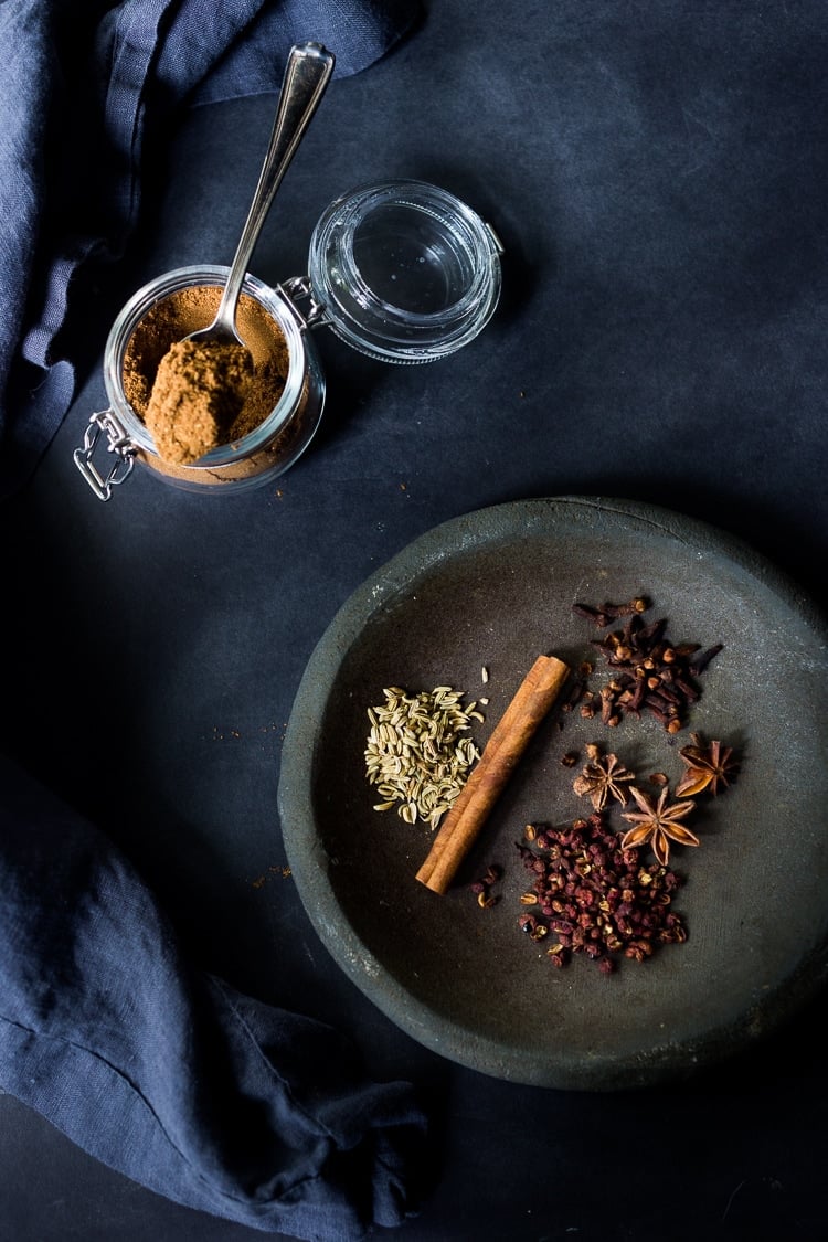 jar with Chinese Five spice with spoon, beside small dish with whole spices- fennel seeds, star anise, cinnamon stick, cloves, and szechuan peppercorns.